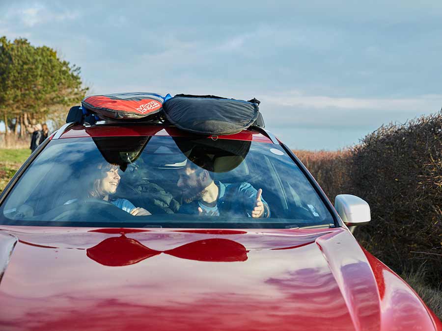 Save 15% plus £20 fuel voucher, couple driving on holiday in a red car